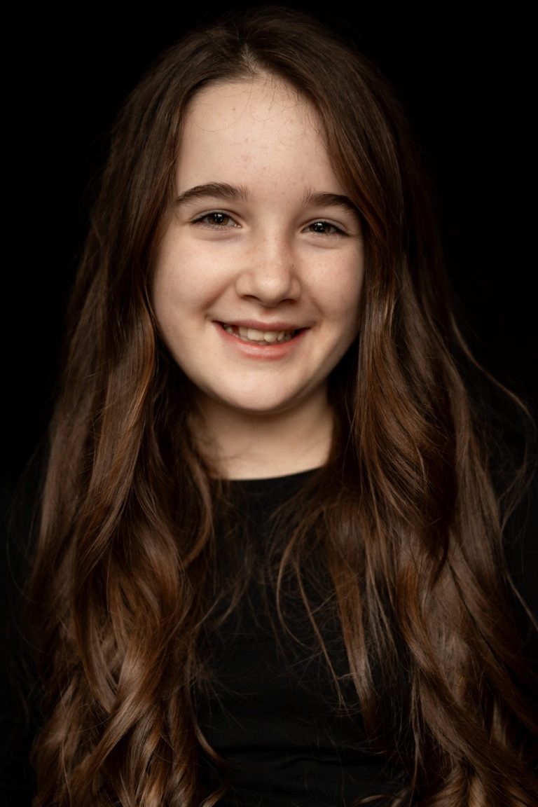 Meisje met lang, bruin haar en een glimlach, gekleed in zwart shirt.