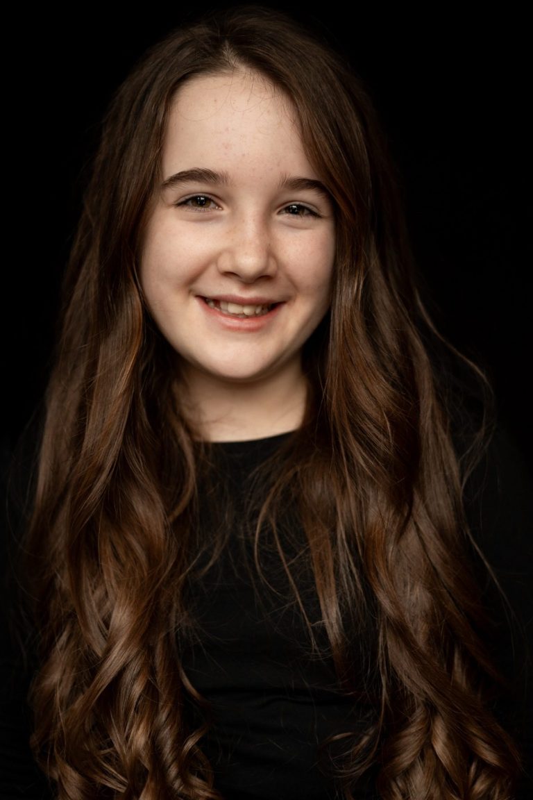 Meisje met lang bruin haar en een glimlach, gekleed in zwart.