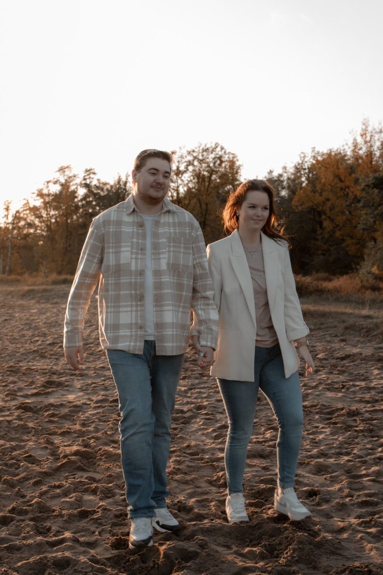 Een paar wandelt hand in hand over een zandige ondergrond bij zonsondergang.