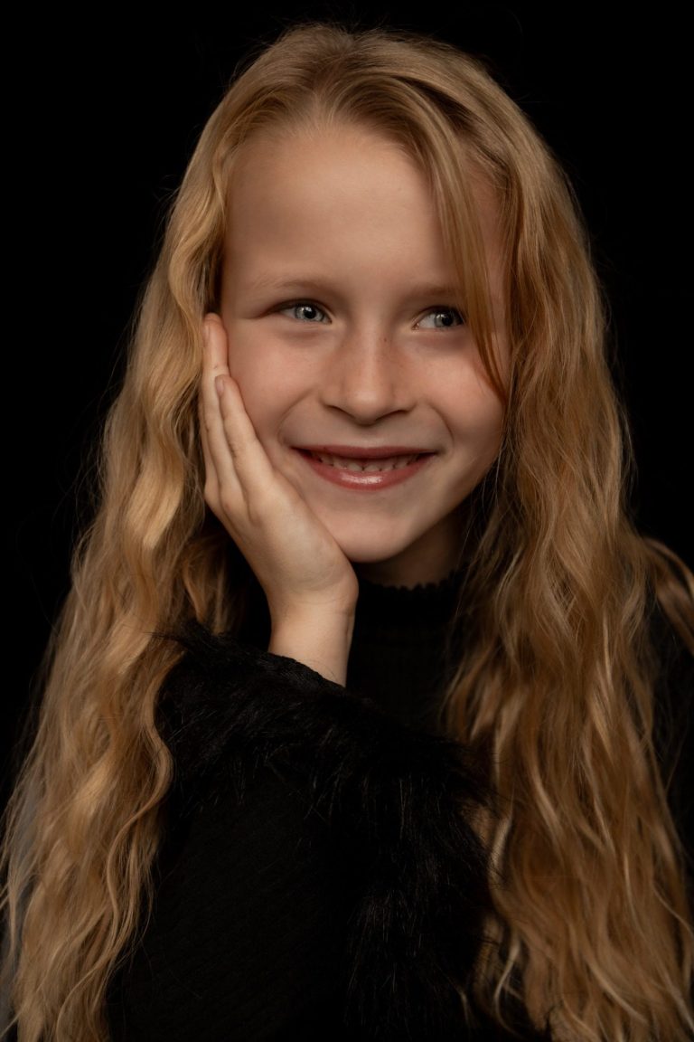 Een glimlachend meisje met lang, blond haar en een zwarte kledingstuk.