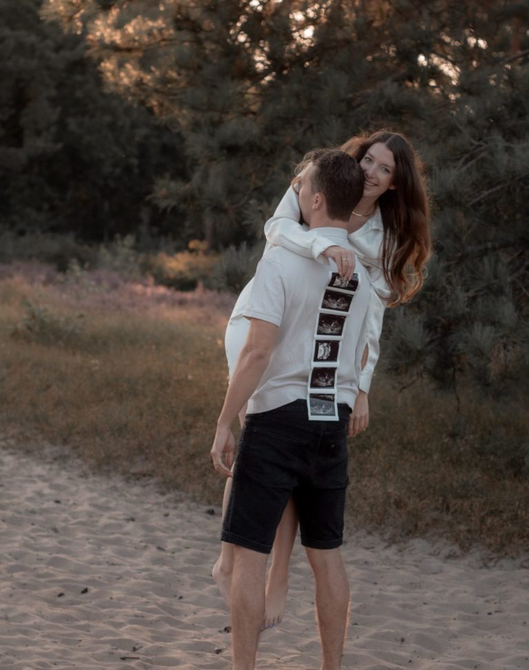 Jong stel op een strand, vrouw omhelst man vanaf zijn rug met een zonnige achtergrond.
