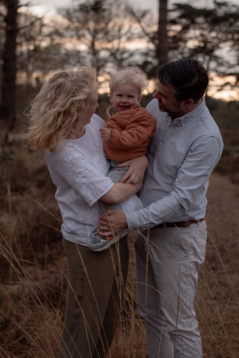 Gezin buiten, ouders houden een peuter vast in een natuuromgeving bij zonsondergang.
