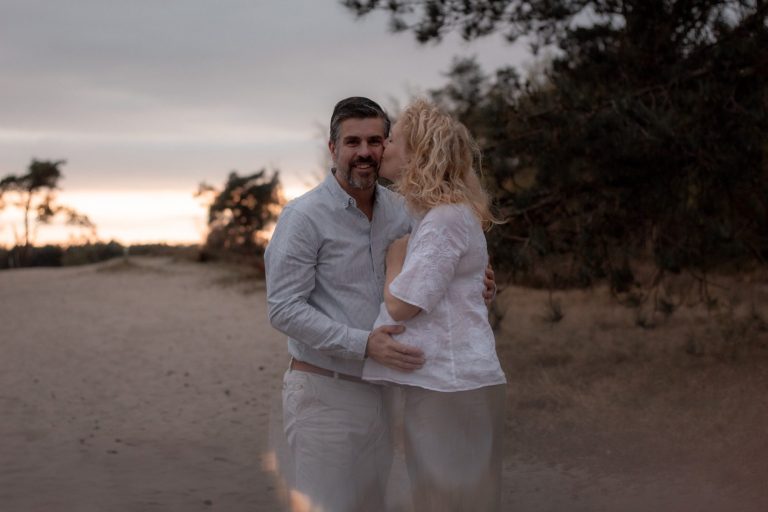 Twee mensen omhelzen elkaar op een zandpad tijdens zonsondergang.