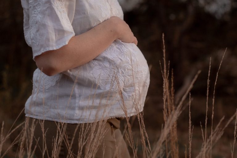 Vrouw met een zichtbare zwangere buik, omringd door gras.