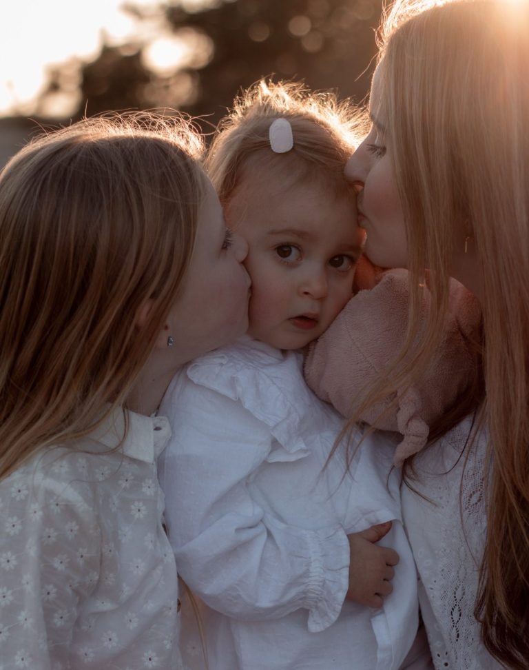Een moeder kust haar twee kinderen, omringd door een warme gouden gloed.