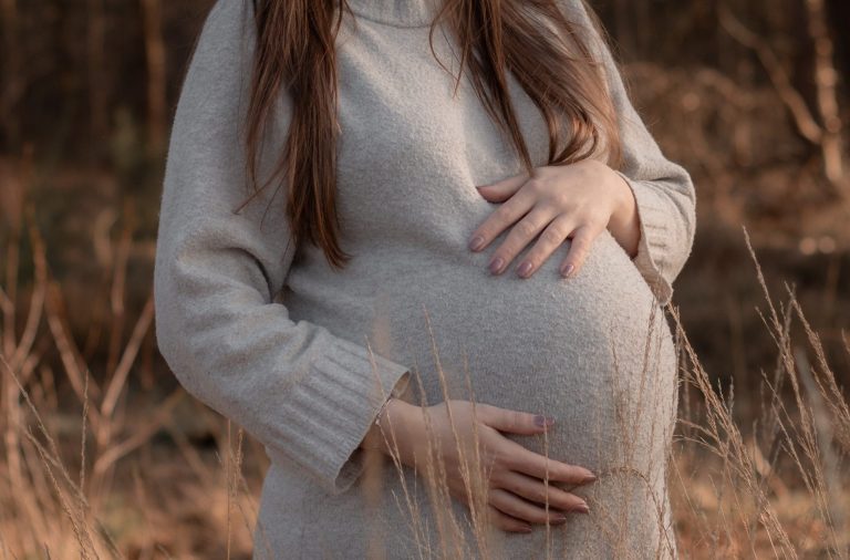 Een zwangere vrouw met lange haren in een natuurlijke omgeving.