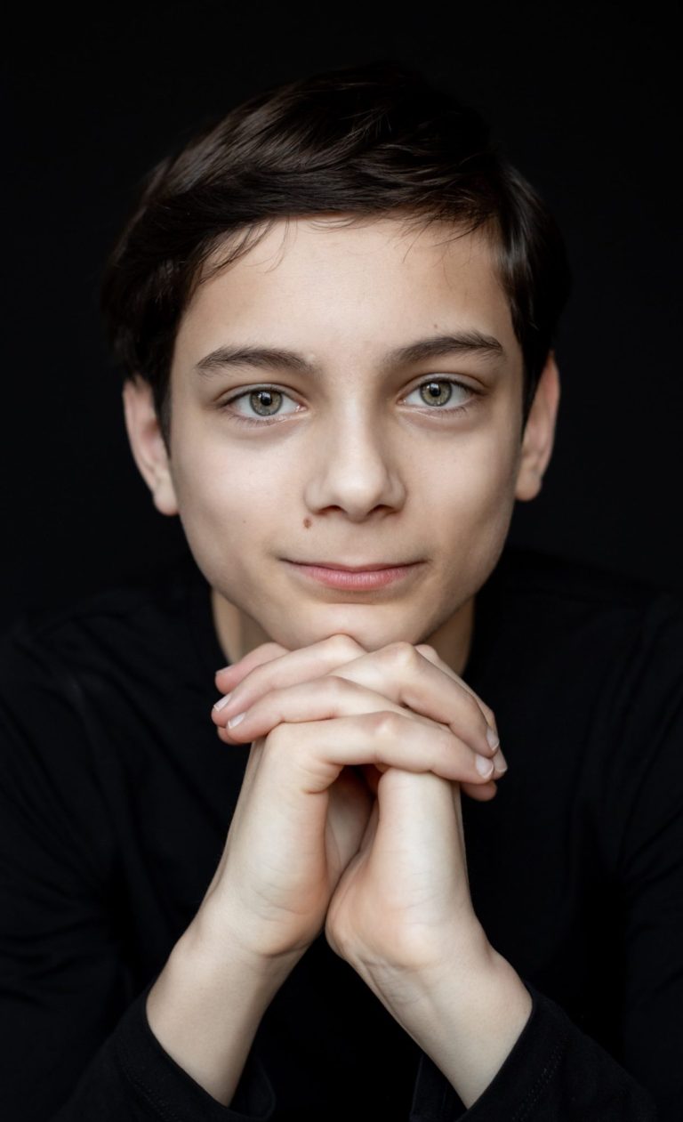 Meisje met lange haren, leunt met de handen op haar kin en kijkt nadenkend.