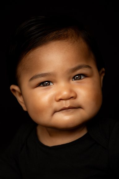 Een glimlachende baby met een donkere huid en kort, steil haar op een zwarte achtergrond.