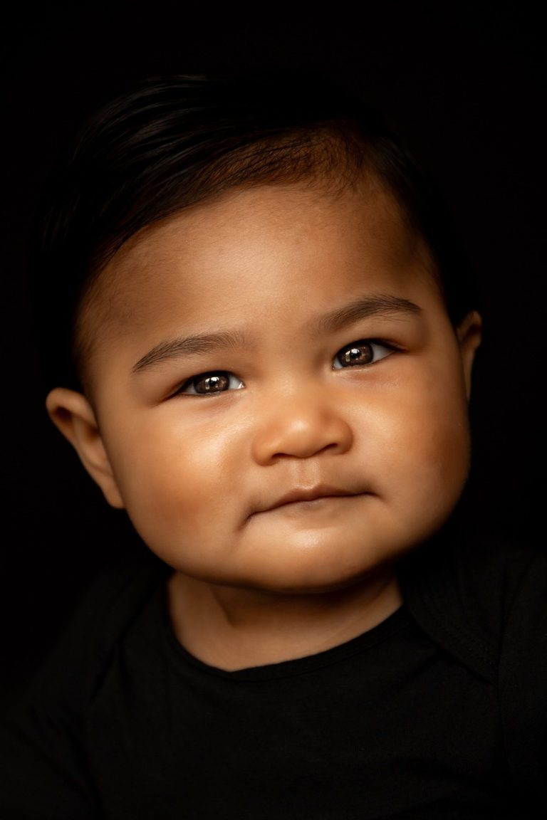 Een glimlachende baby met een donkere huid en kort, glad haar.