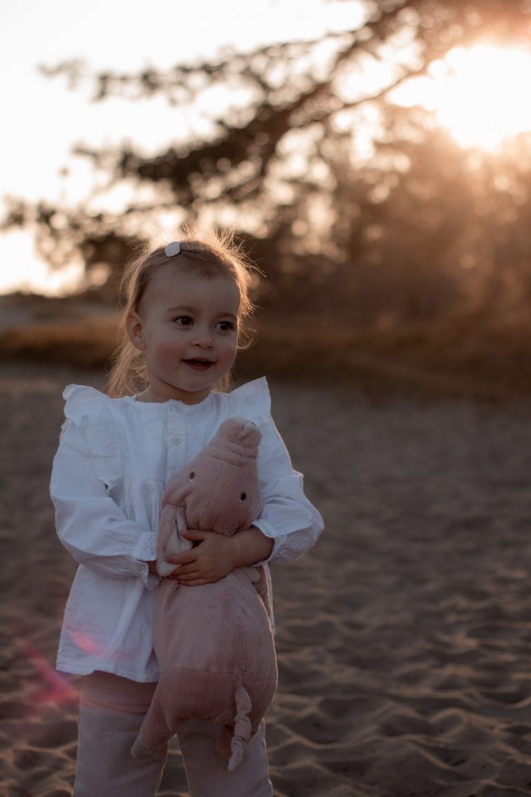 Een meisje in een witte blouse houdt een knuffel varken vast, omringd door zonlicht.