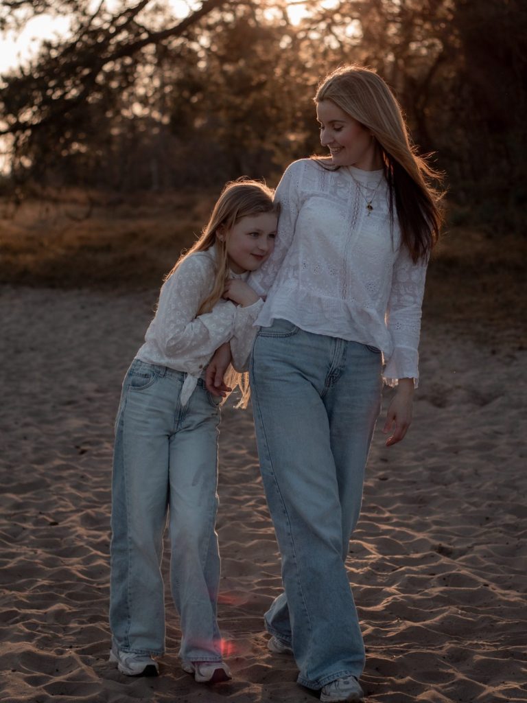 Moeder en dochter wandelen samen op het strand tijdens zonsondergang.