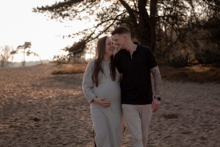 Gelukkige zwangere vrouw en man wandelen samen op een zandige locatie met bomen.