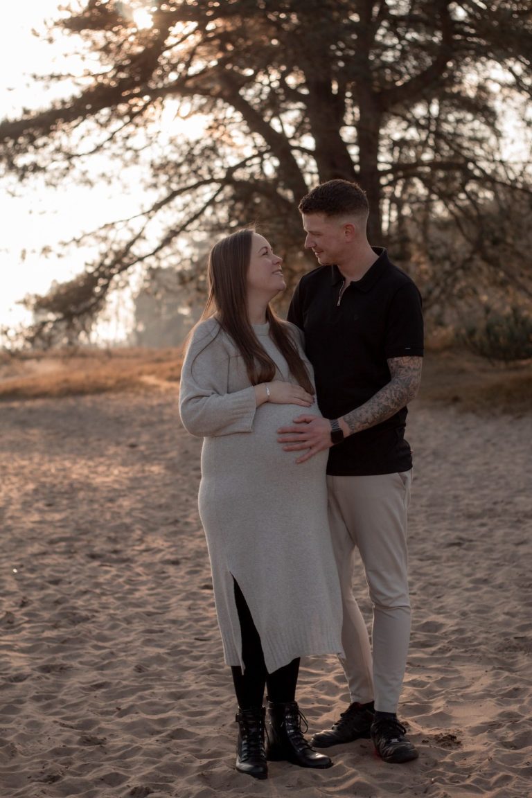 Een paar omhelst elkaar op het strand, met bomen op de achtergrond tijdens zonsondergang.