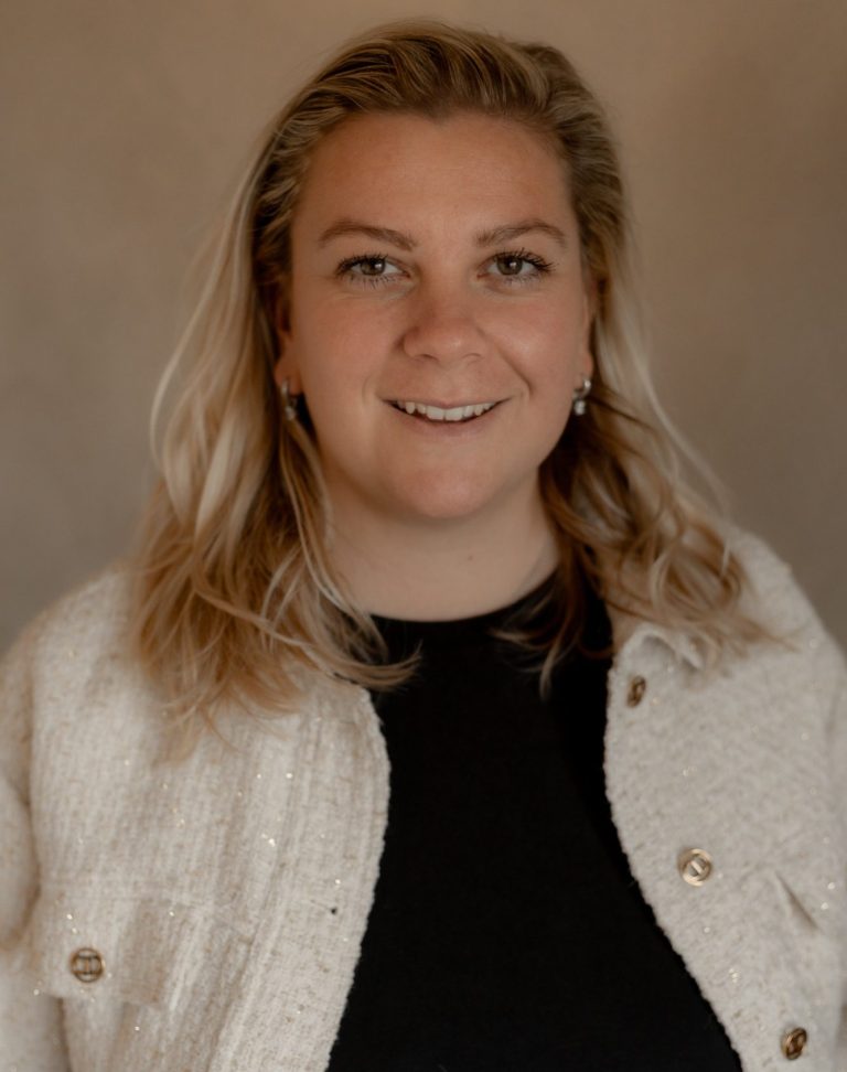 Vrouw met lang, blond haar en een lichte trui, glimlachend naar de camera.