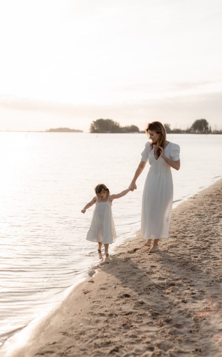 Twee meisjes lopen samen op het strand, omarmend met een zonsondergang op de achtergrond.