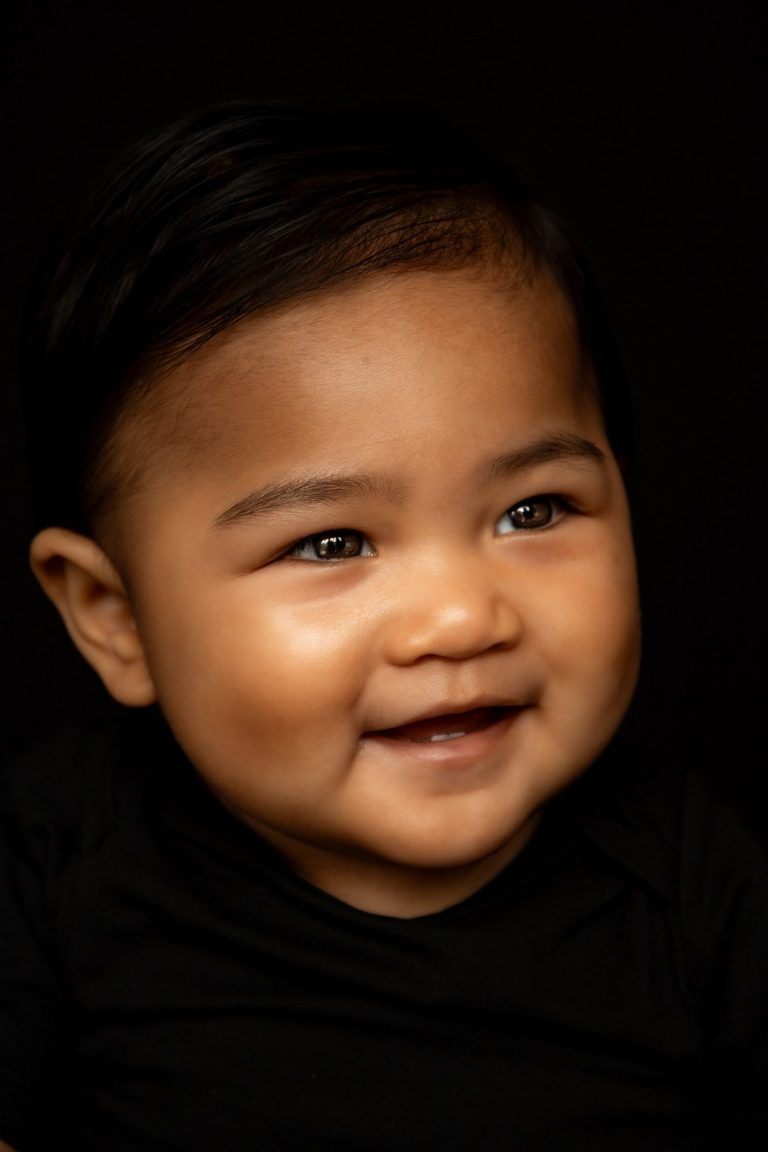 Lachend baby met kort, steil haar op een donkere achtergrond.