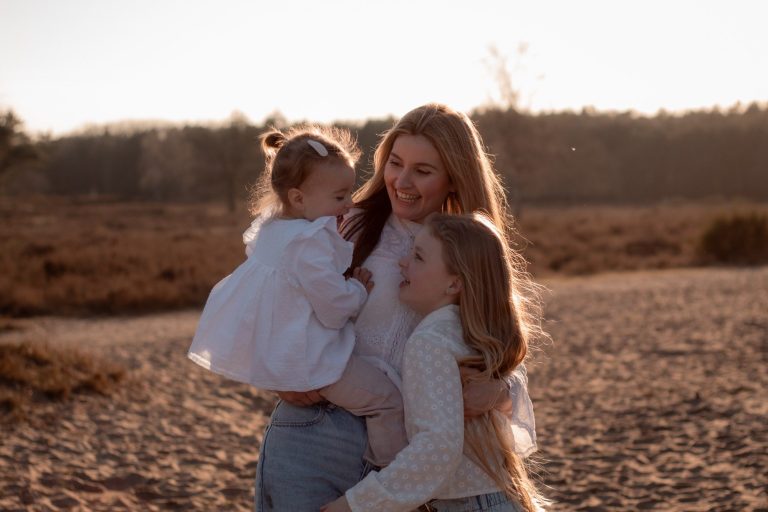 Moeder omarmt haar twee dochters in een natuurlijke omgeving tijdens zonsondergang.