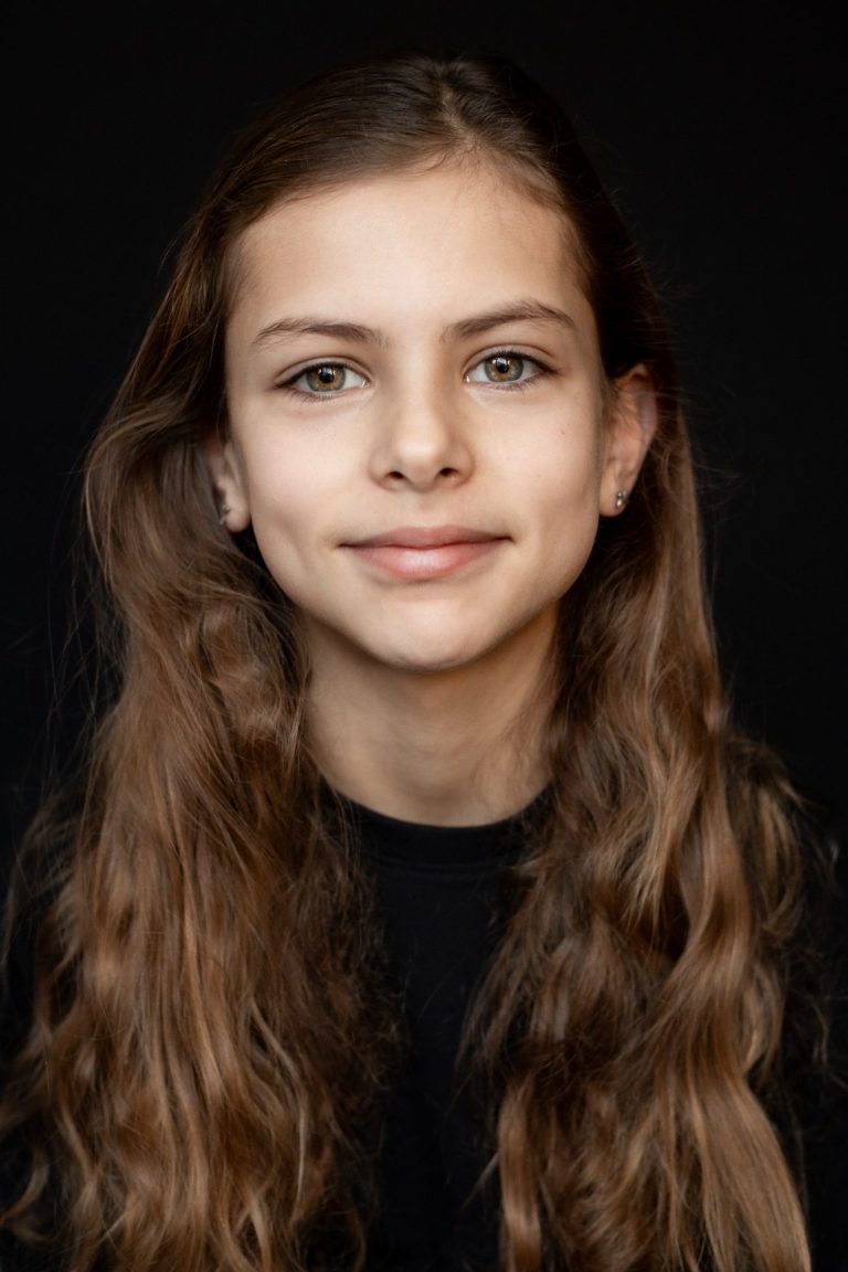 Een jong meisje met krullend haar en een glimlach, gekleed in het zwart.