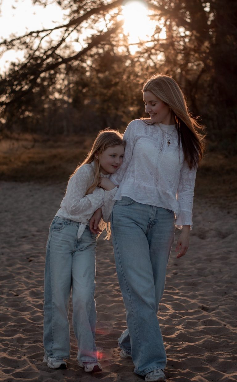 Twee meisjes lopen samen op het strand, omarmend met een zonsondergang op de achtergrond.