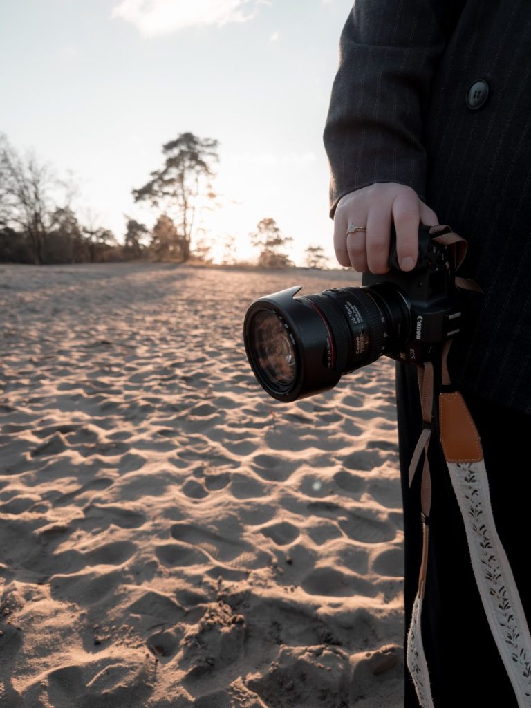 Een fotograaf legt een stel vast op het zand, met bomen op de achtergrond.