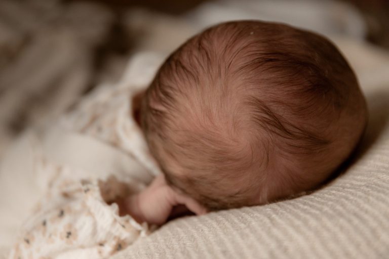 Babyhoofdje met fijn haar, liggend op een lichte, zachte ondergrond.